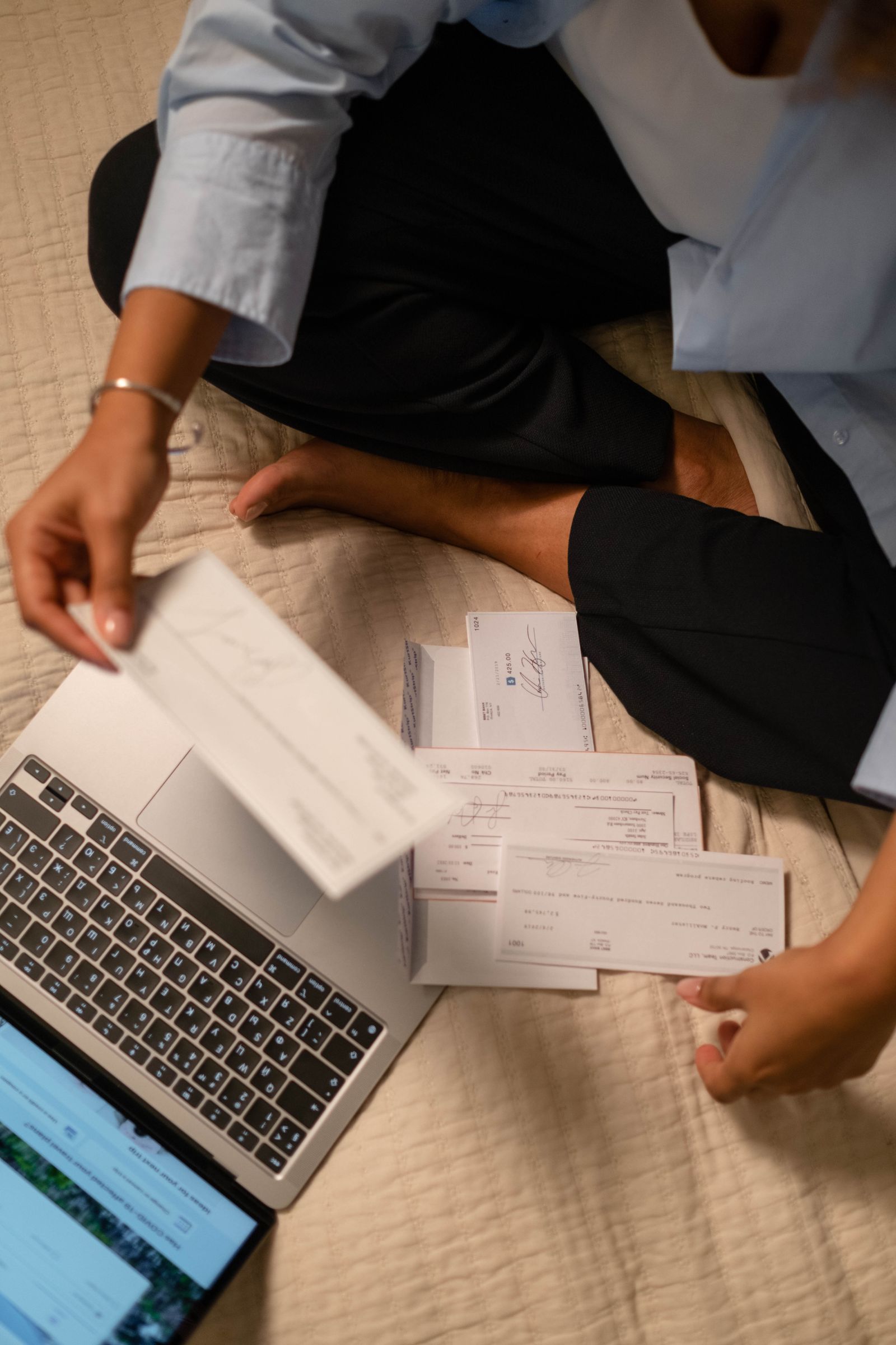 Person verwaltet Finanzen mit Laptop und Belegen auf einer Decke